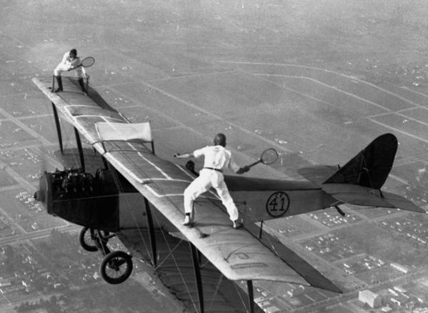 Professional airwalkers Gladys Roy and Ivan Unger playing tennis on the wing of a biplane in-flight, 1925