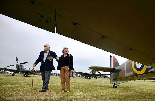 Battle of Britain veteran pilot Tony Pickering and his wife, Chris, walk between a Spitfire [L) and Hurricane aircraft